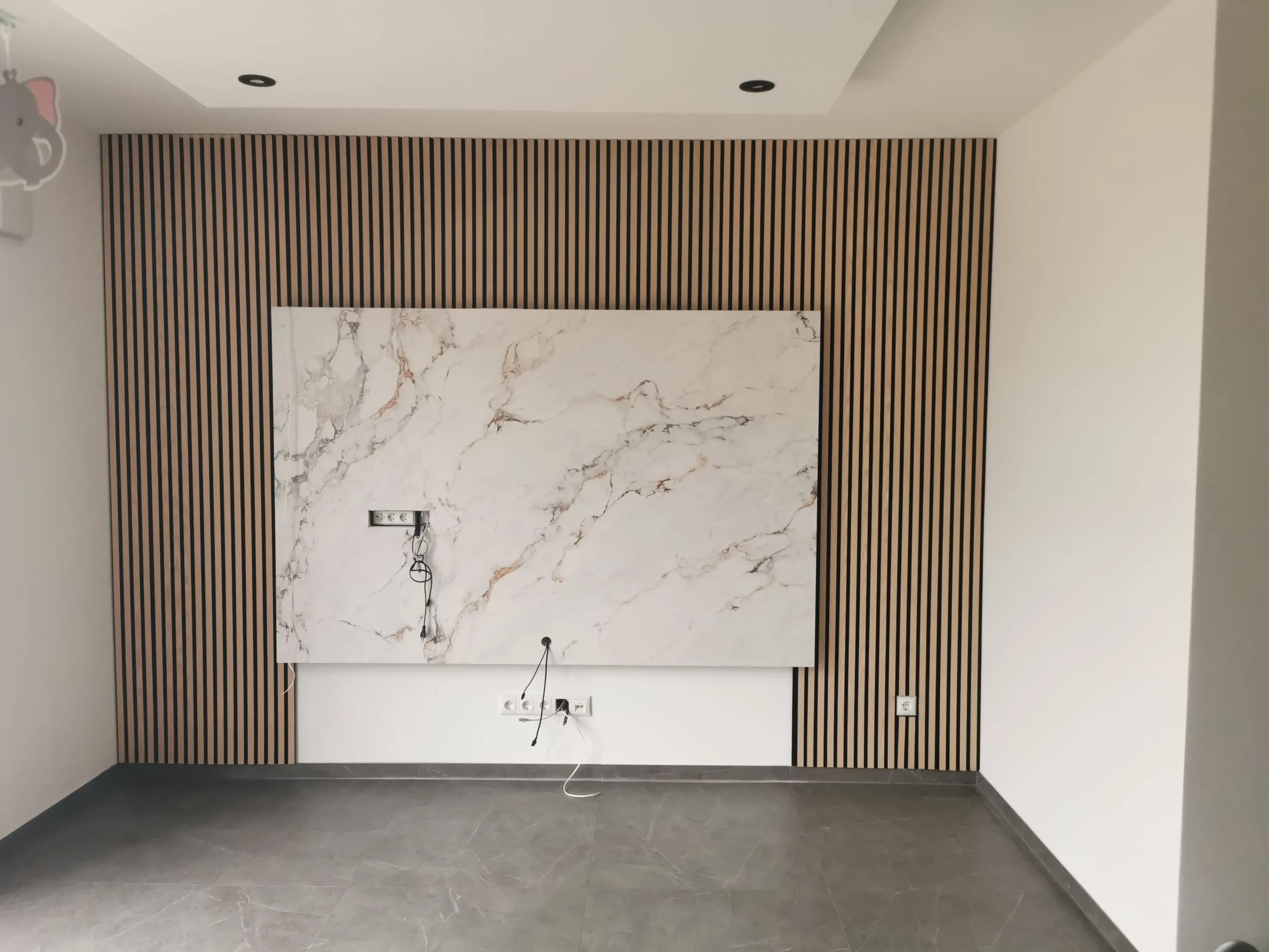 Wohnraum mit Akustik-Holzlamellenwand, großformatiger Marmorplatte und abgehängter Decke mit Einbauspots